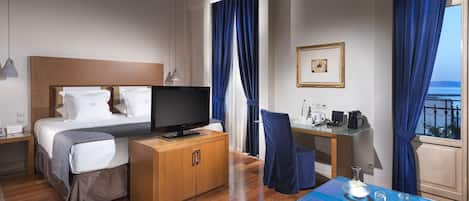 Una habitación de hotel con cama, televisor, escritorio y vista al mar.