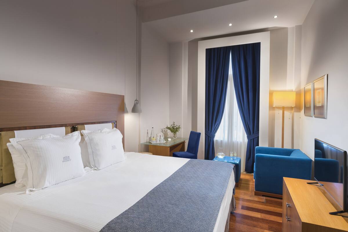 A hotel room with a large bed, a desk, a chair, and a TV.