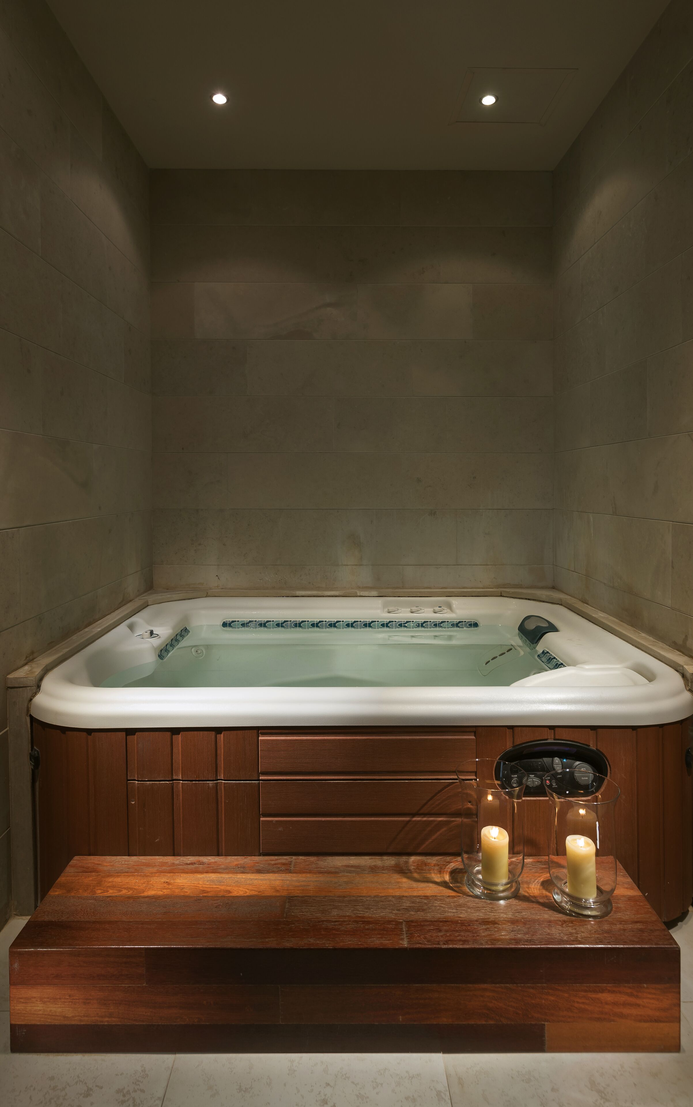 A spa room with a hot tub, wooden paneling, and two candles on a wooden table.
