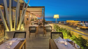 Un espace extérieur aménagé pour les repas, avec des tables pour deux personnes, offrant une vue sur la côte.