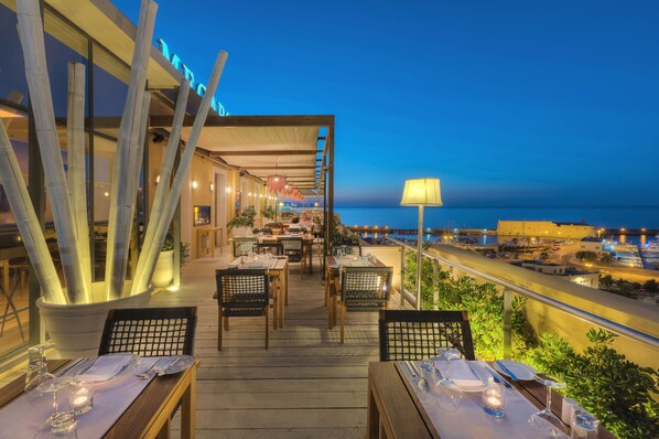 An outdoor dining area with tables set for two, overlooking a coastal view.