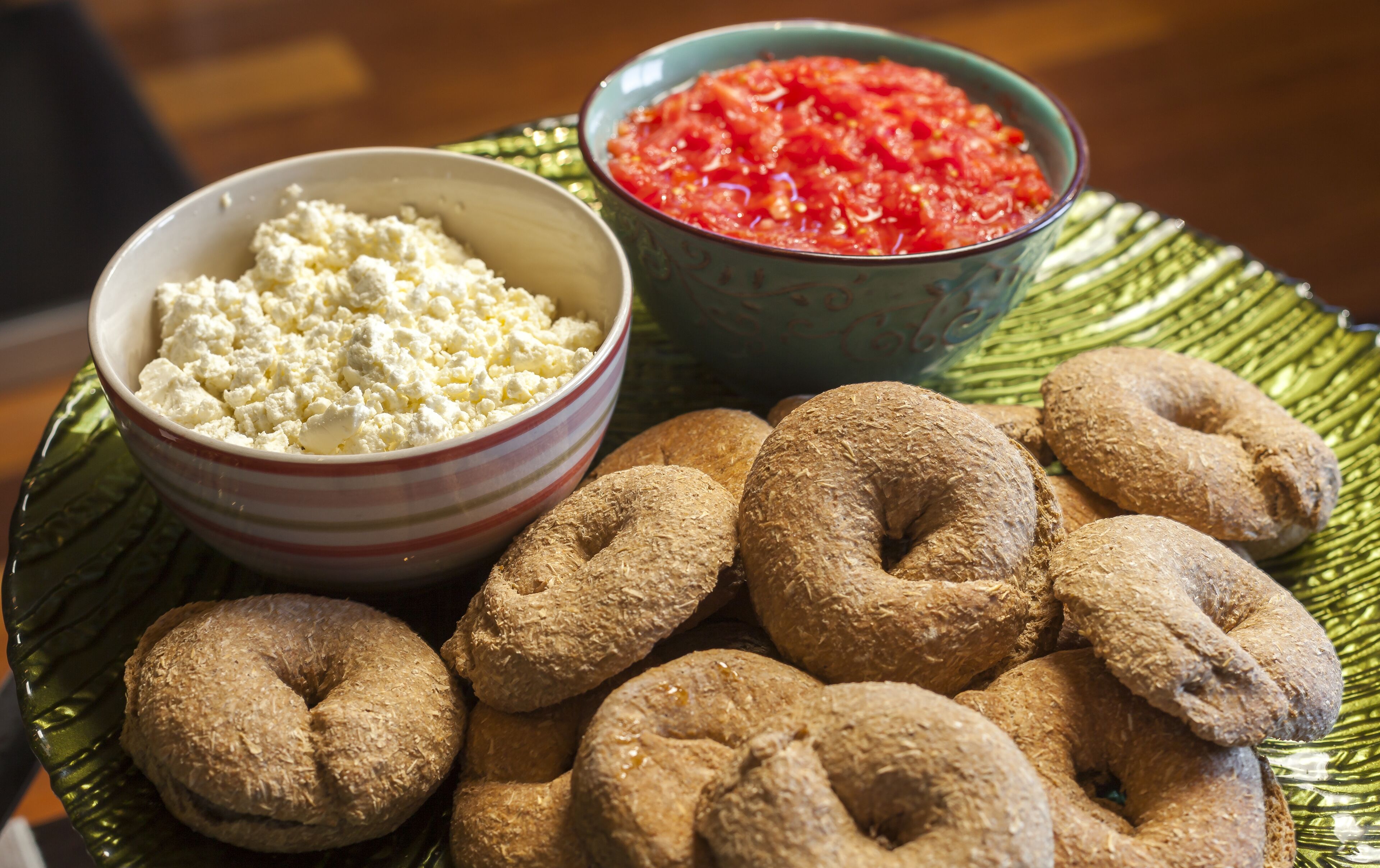 Ein Teller mit einer Schüssel Hüttenkäse, einer Schüssel Tomatensauce und mehreren Vollkorn-Bagels.