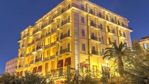 Un hôtel à plusieurs étages doté de balcons, avec un palmier au premier plan et une enseigne lumineuse.