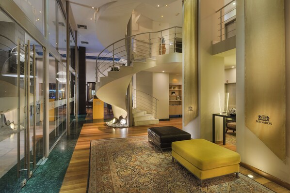 A modern interior with a spiral staircase, a yellow ottoman, and a large rug. - GDM Megaron Historical Monument Hotel (Heraklion)