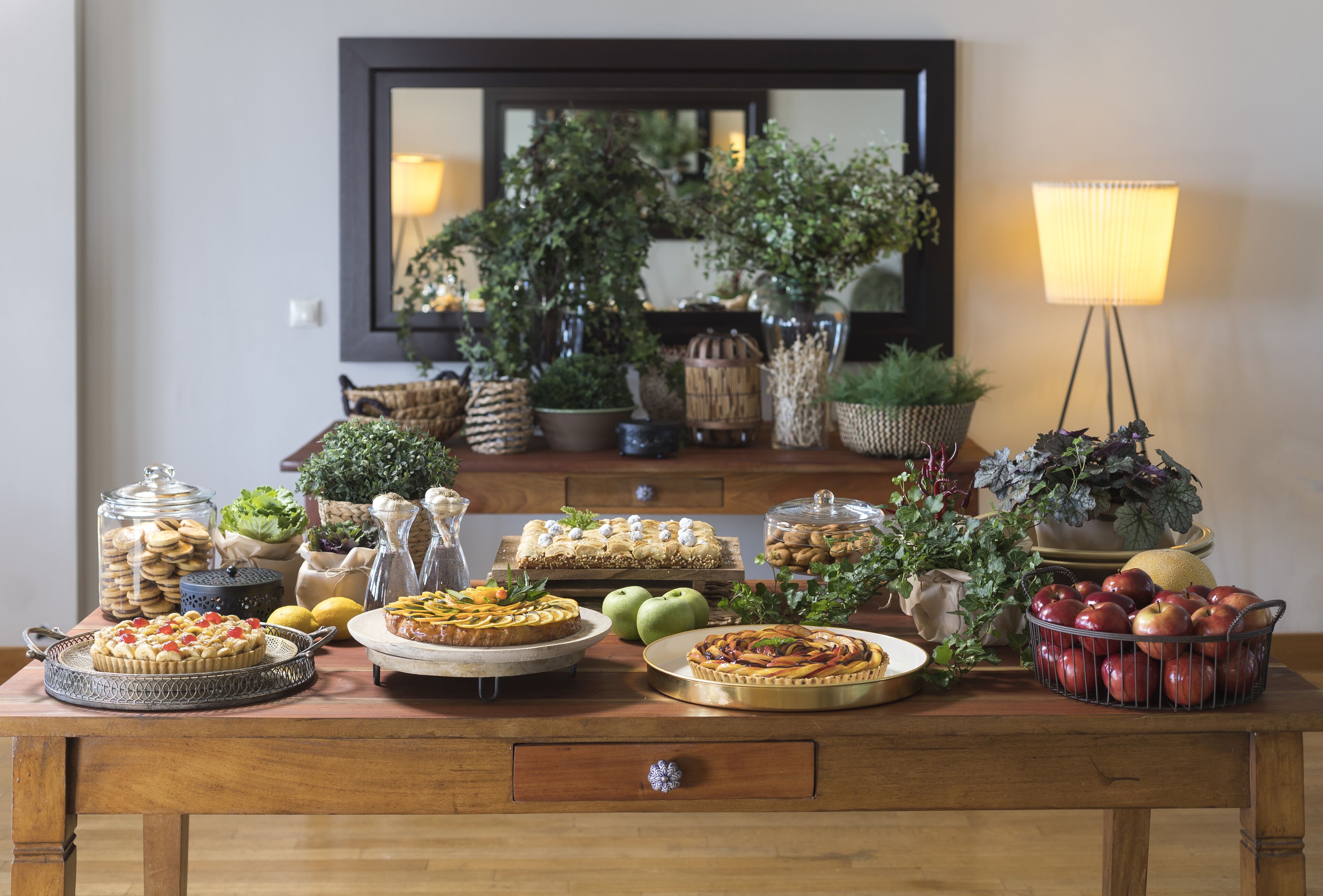 A wooden table with various food items, including pies and apples, and decorative plants.
