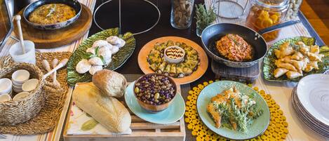 Een tafel met diverse etenswaren en gerechten, waaronder schalen olijven, een bord brood en een pan met een gerecht.