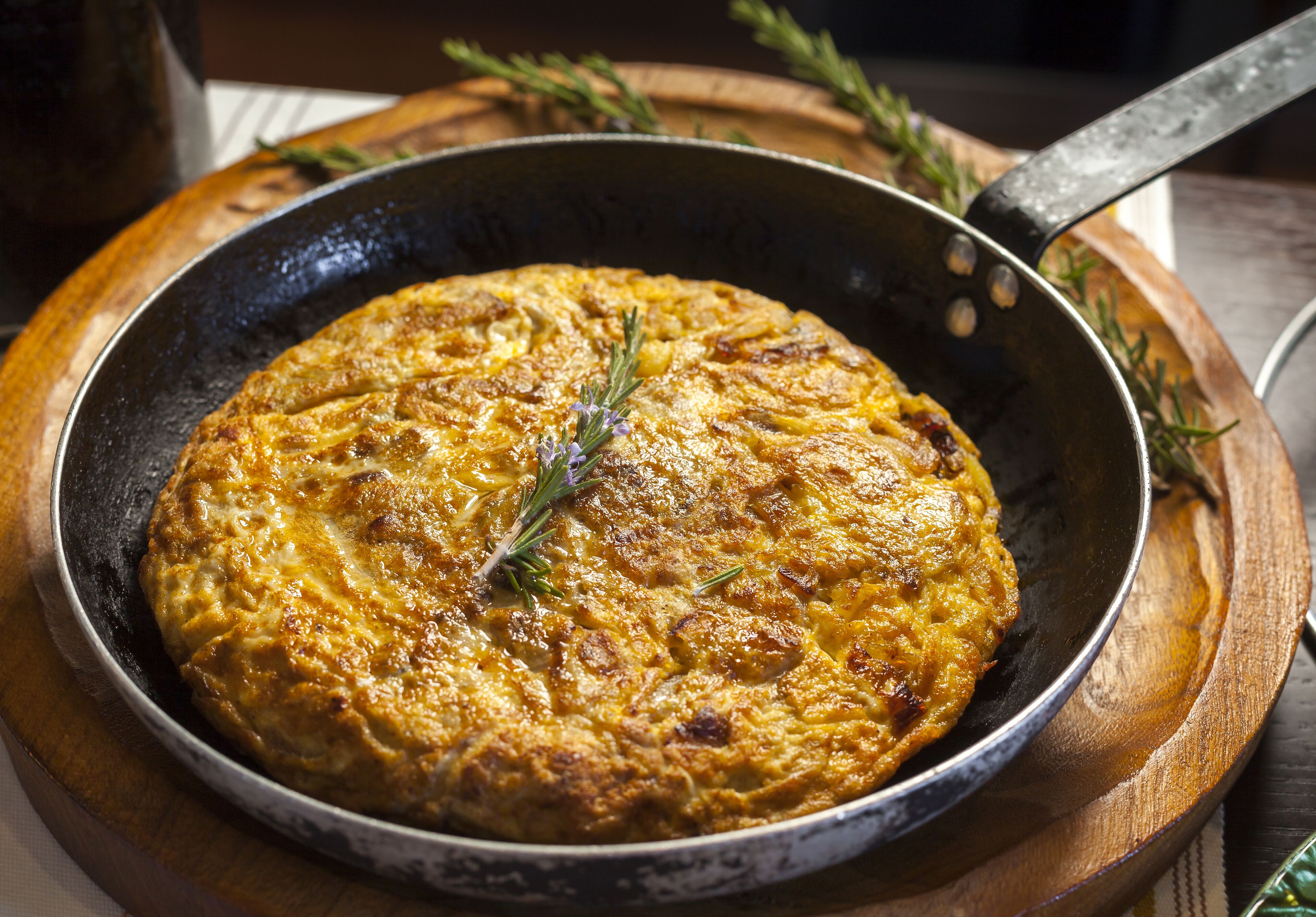 A skillet with a golden-brown dish, possibly a frittata, garnished with a sprig of rosemary.