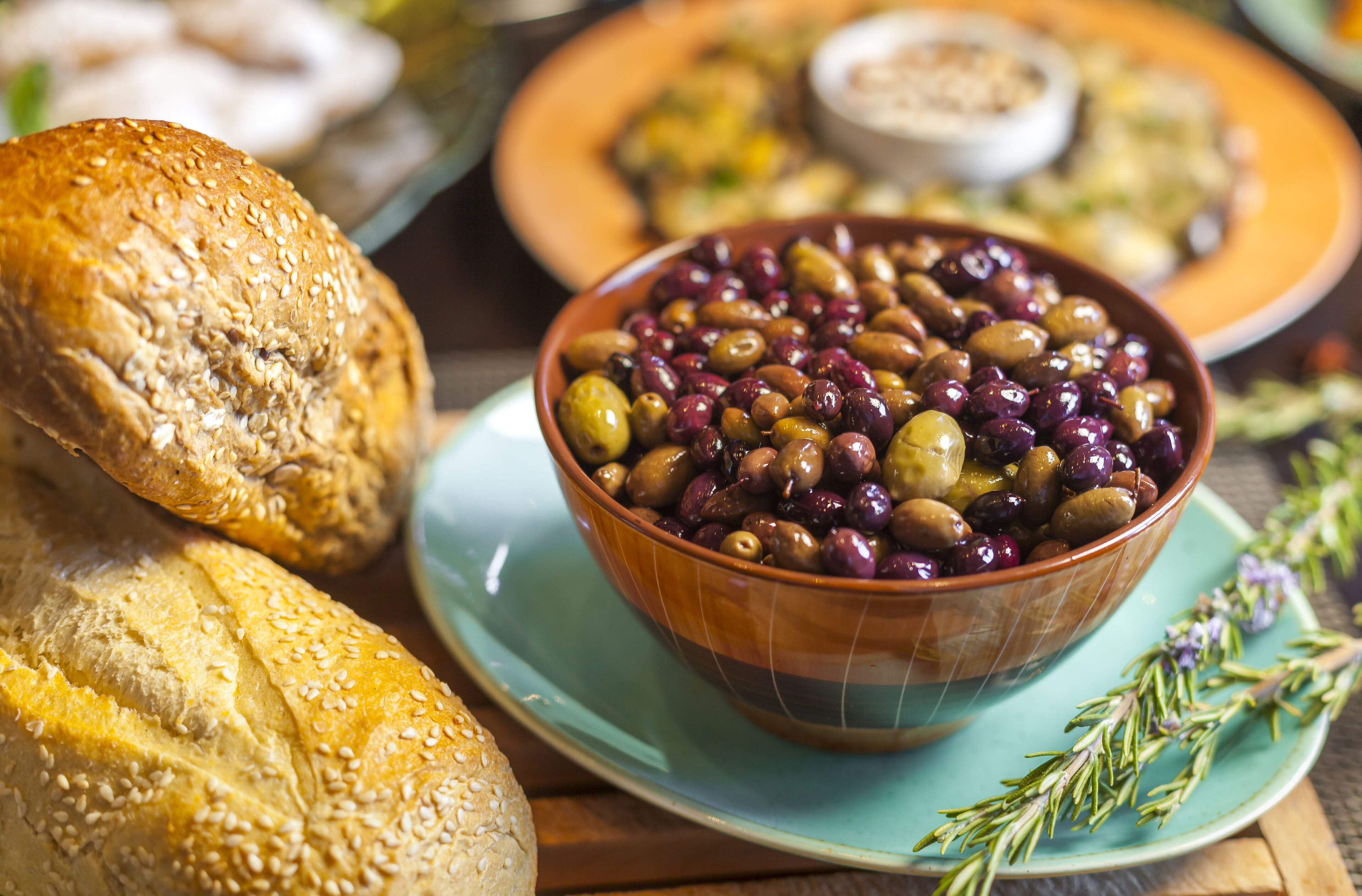 Un bol d’olives sur une assiette, accompagné d’une miche de pain.