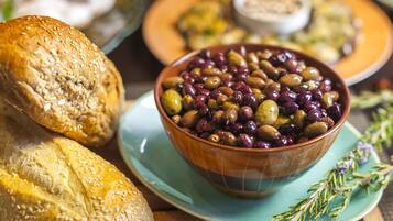 Un bol d’olives sur une assiette, accompagné d’une miche de pain.