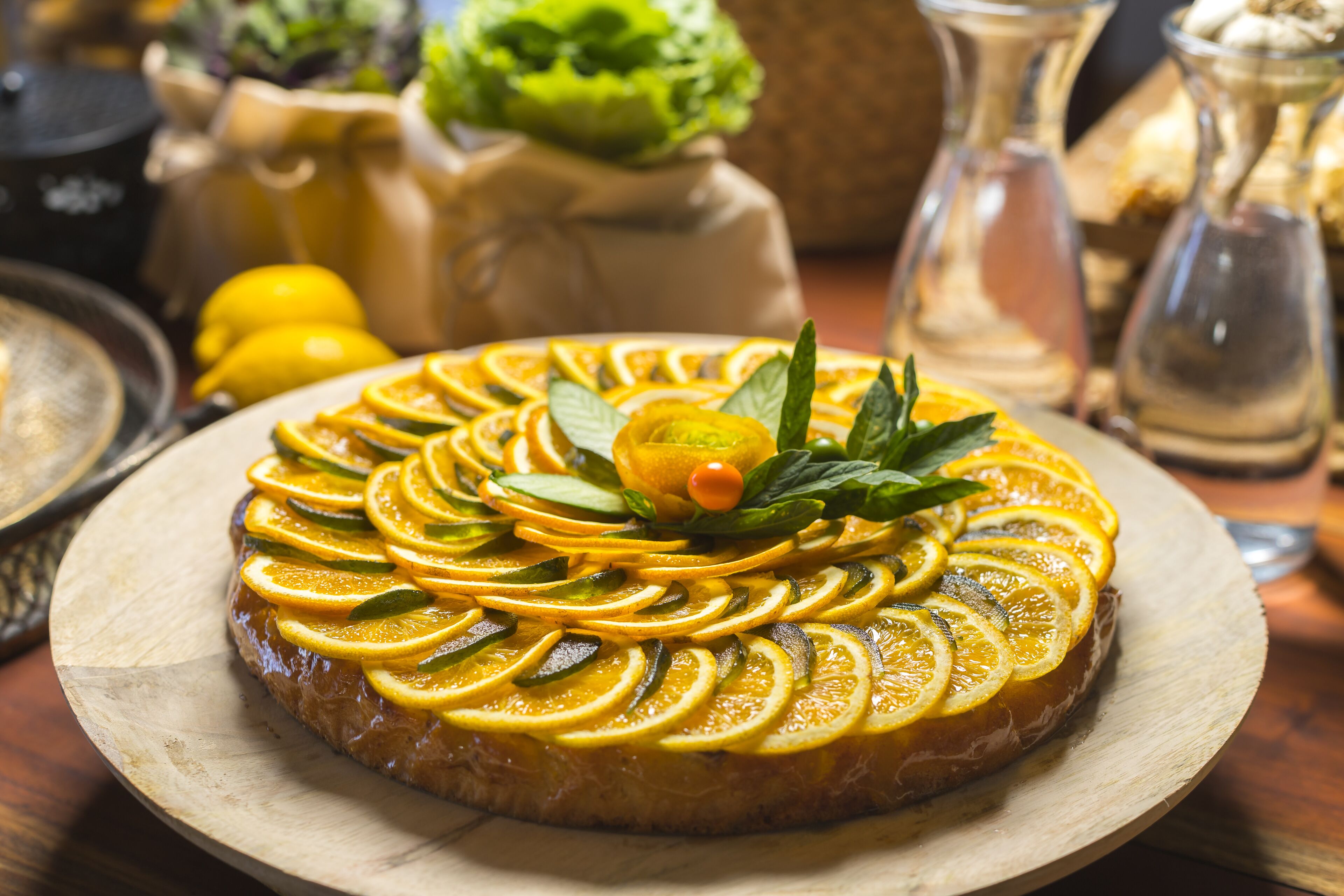Una tarta redonda con rodajas de naranja y hojas de menta sobre una tabla de madera.