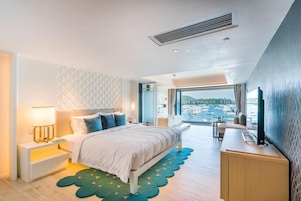 A modern hotel room with a bed, bedside table, lamp, and a view of the sea.