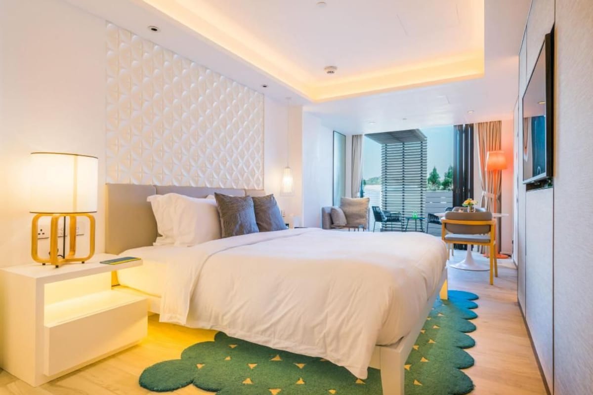 A modern hotel room with a large bed, bedside tables, a desk, and a view of the outdoors.