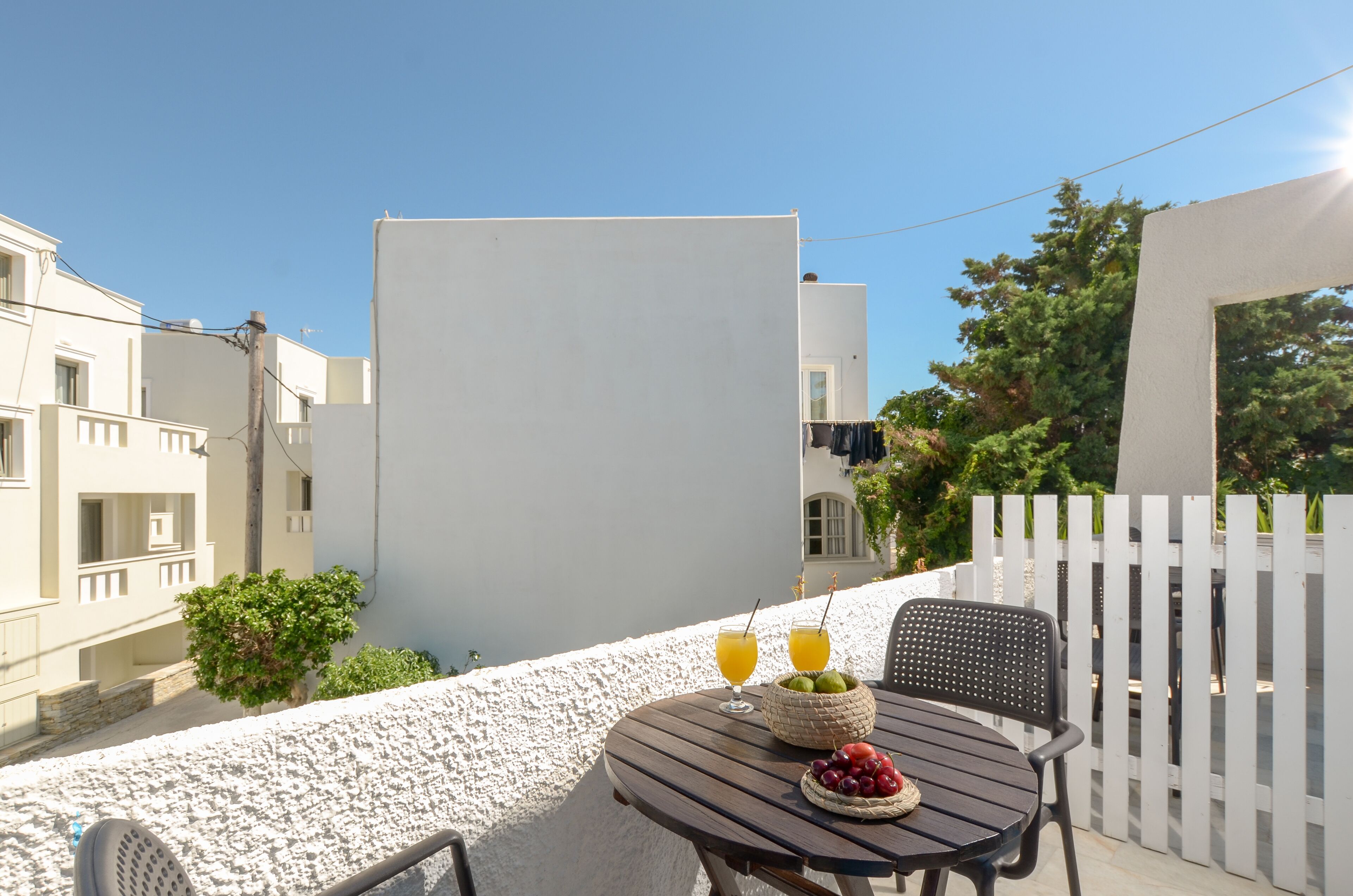 A balcony with a round table, two glasses of orange juice, a basket of cherries, and a wicker bowl.