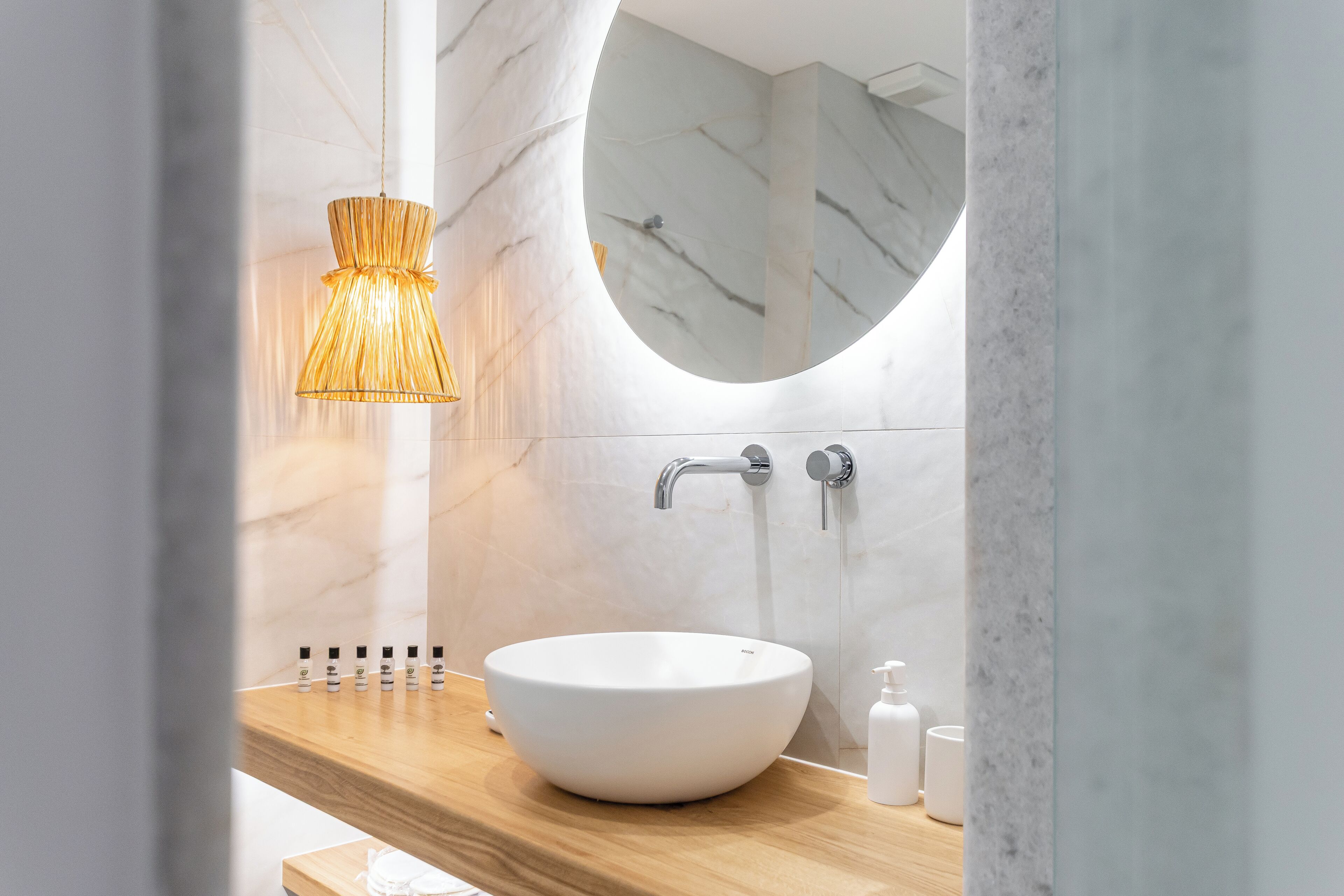 A modern bathroom with a round mirror, a white vessel sink, and a wooden countertop.