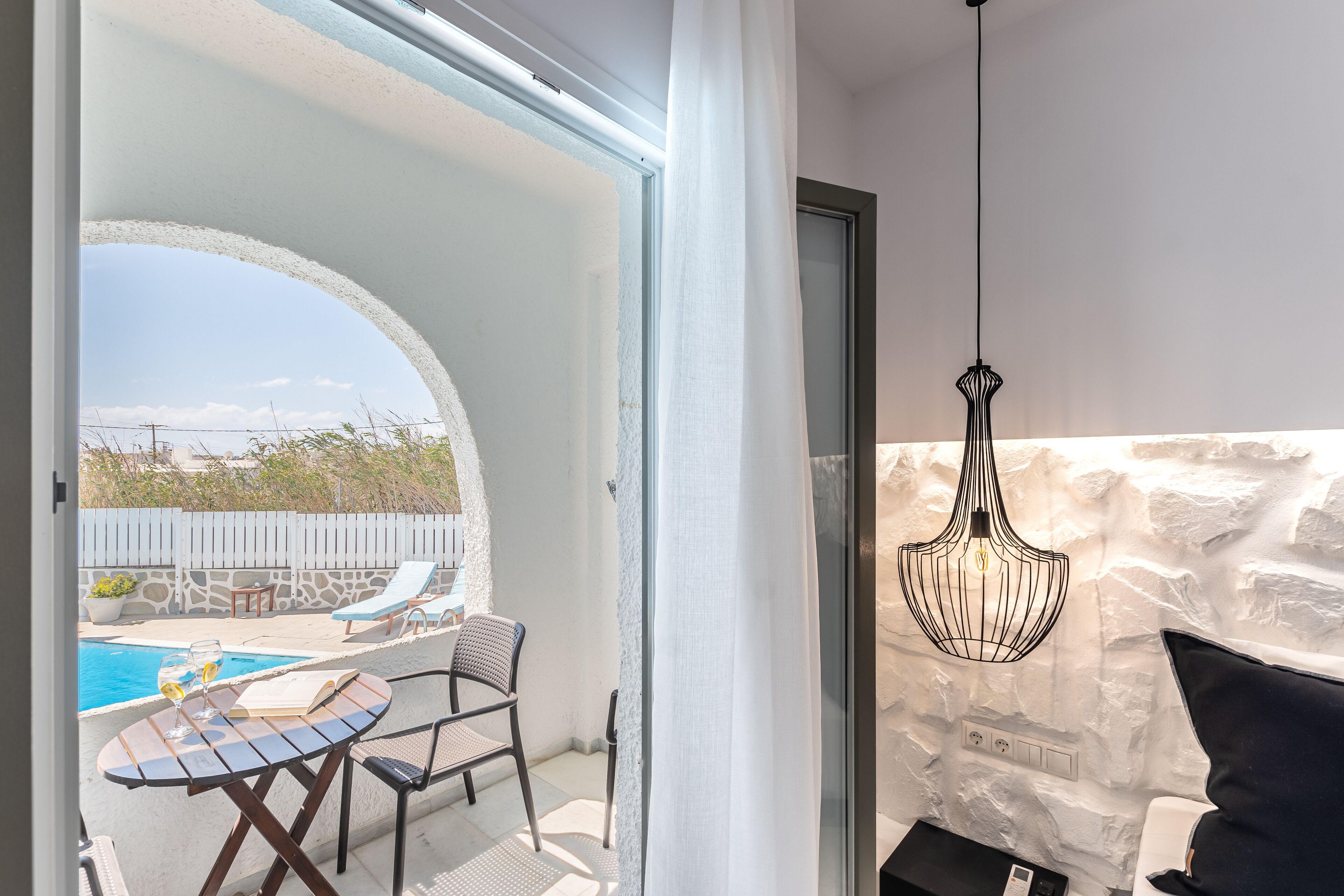 Un balcon avec une piscine, des chaises longues et une table sur laquelle se trouvent un livre et des verres.