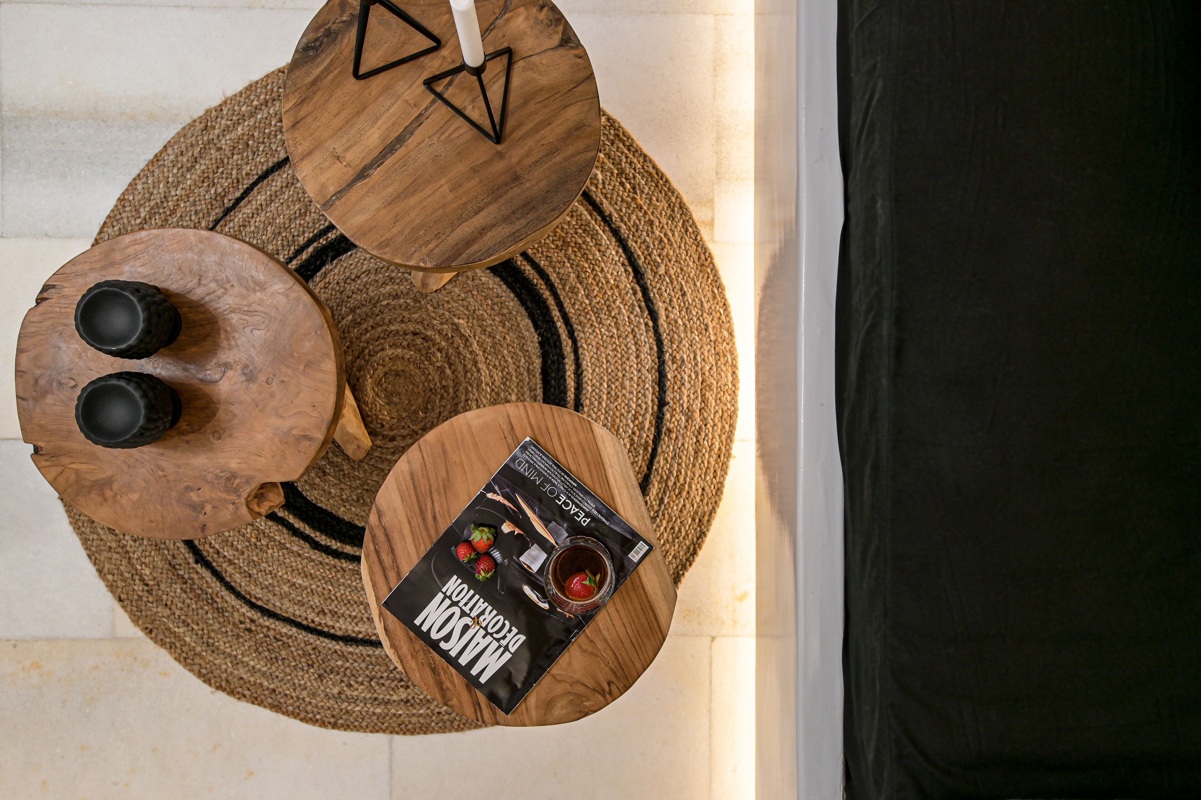 A top-down view of a room with a round wooden table, two black cups, a woven rug, and a magazine on the table.