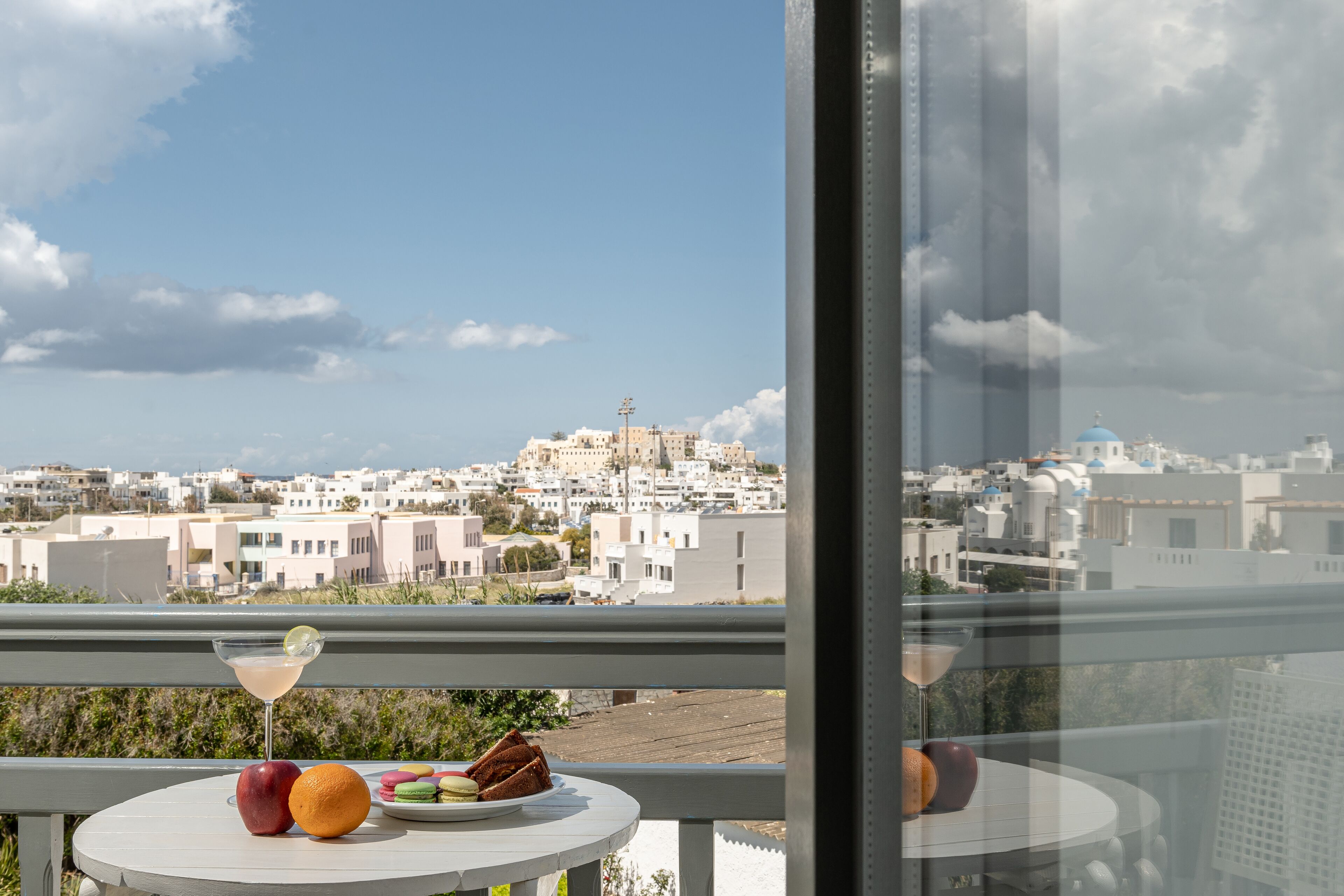 A balcony with a table set for a meal, overlooking a cityscape with white buildings and a distant hill.