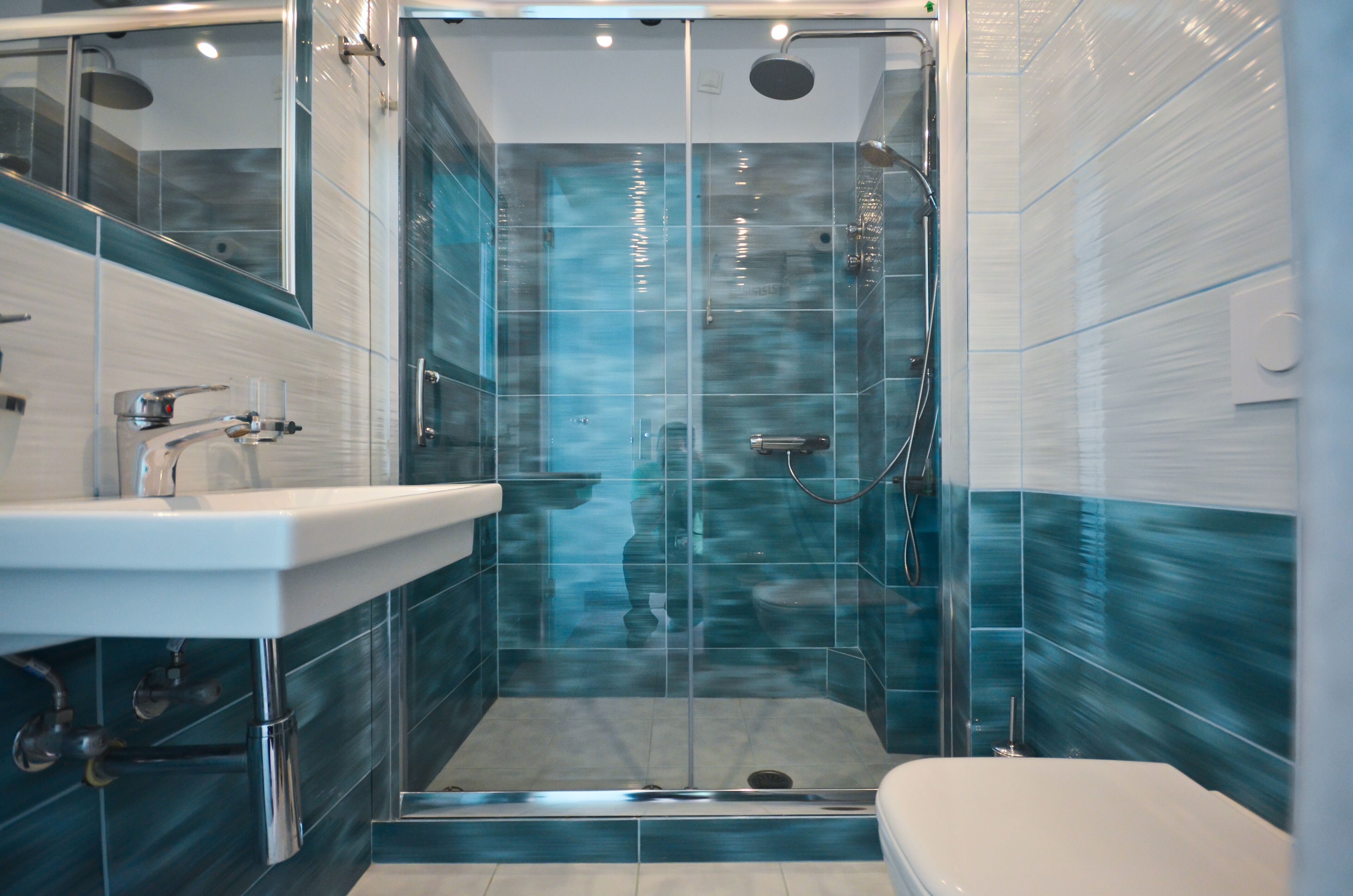 Un baño moderno con ducha envuelta en vidrio, lavamanos blanco y un inodoro.