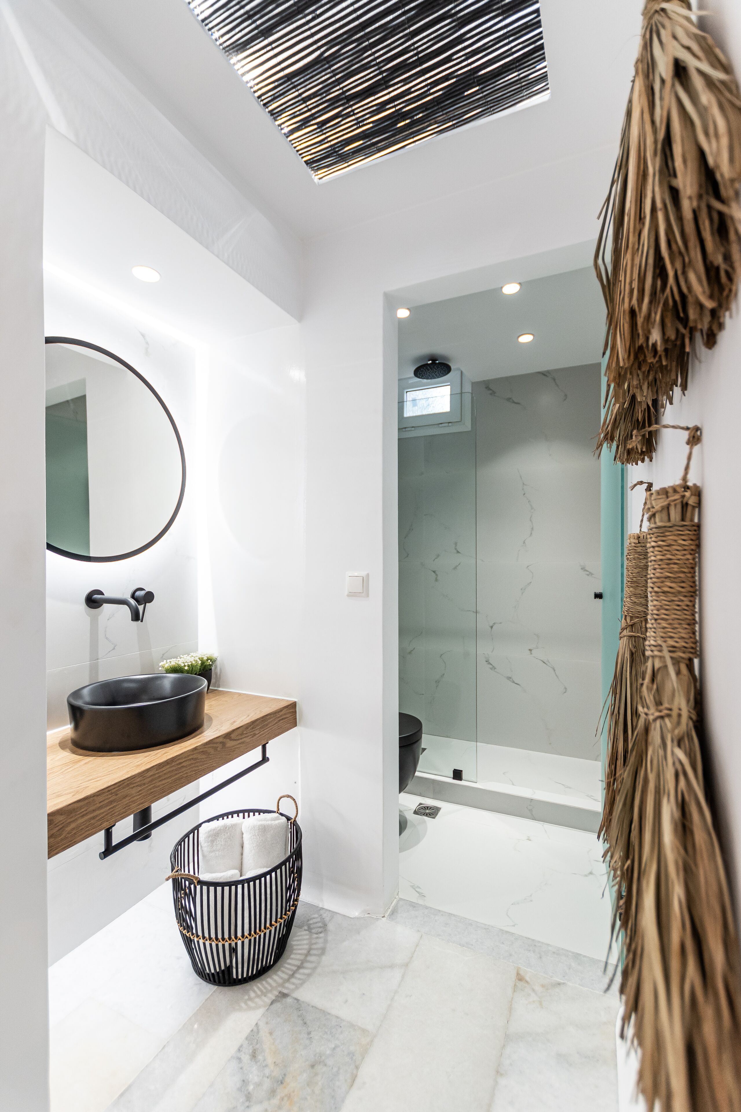 A modern bathroom with a round mirror, black sink, and a glass shower enclosure.