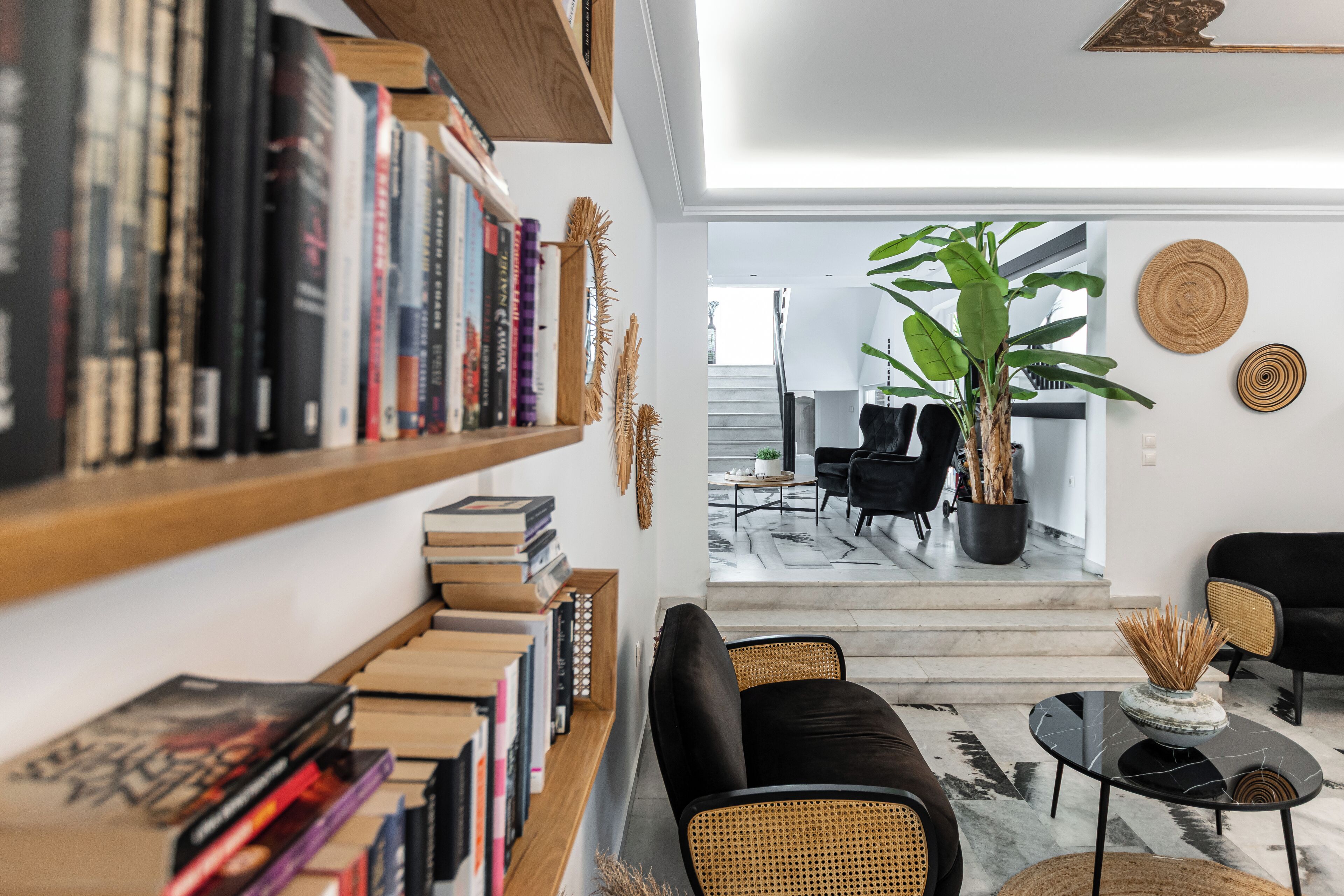 Ein modernes Wohnzimmer mit Bücherregal, schwarzem Sofa und einer großen Pflanze.