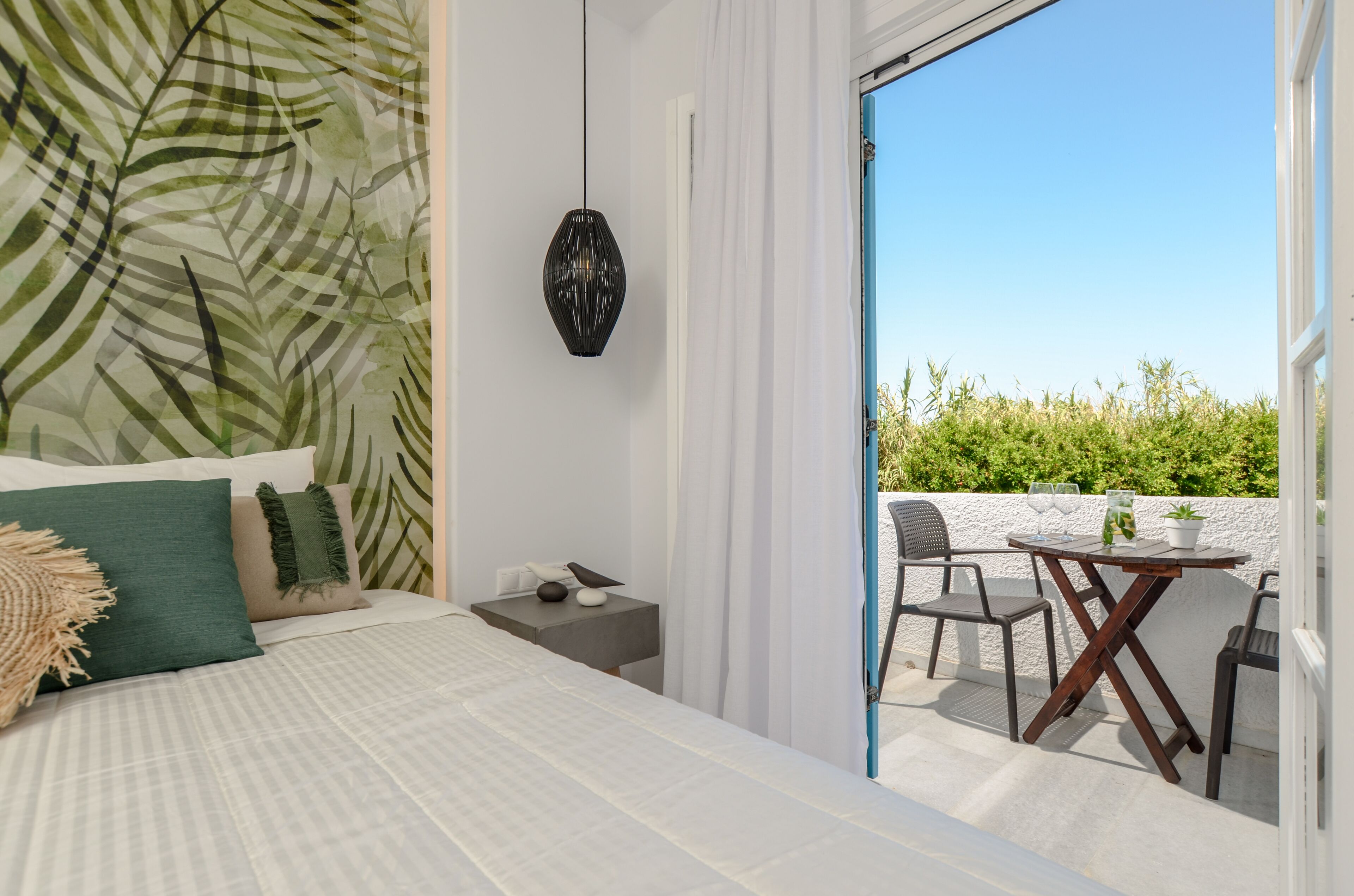 A bedroom with a bed, a nightstand, a hanging lamp, and a balcony with a table and chairs.