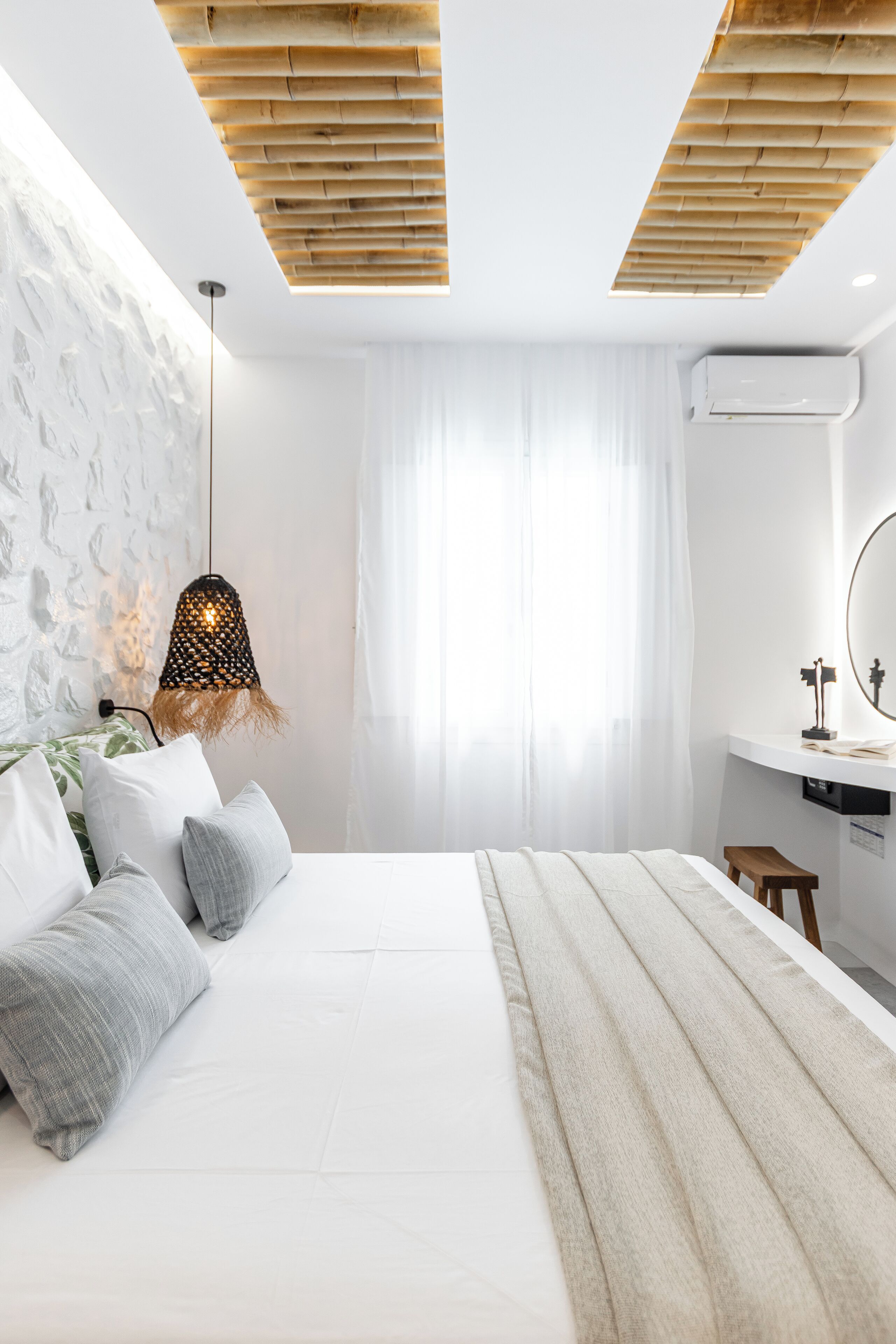 A modern bedroom with a large bed, a bedside table, a hanging lamp, and a window with sheer curtains.
