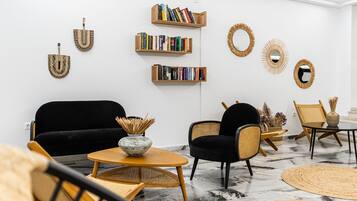 A modern living room with a black sofa, wicker chairs, a round table, and bookshelves with books.