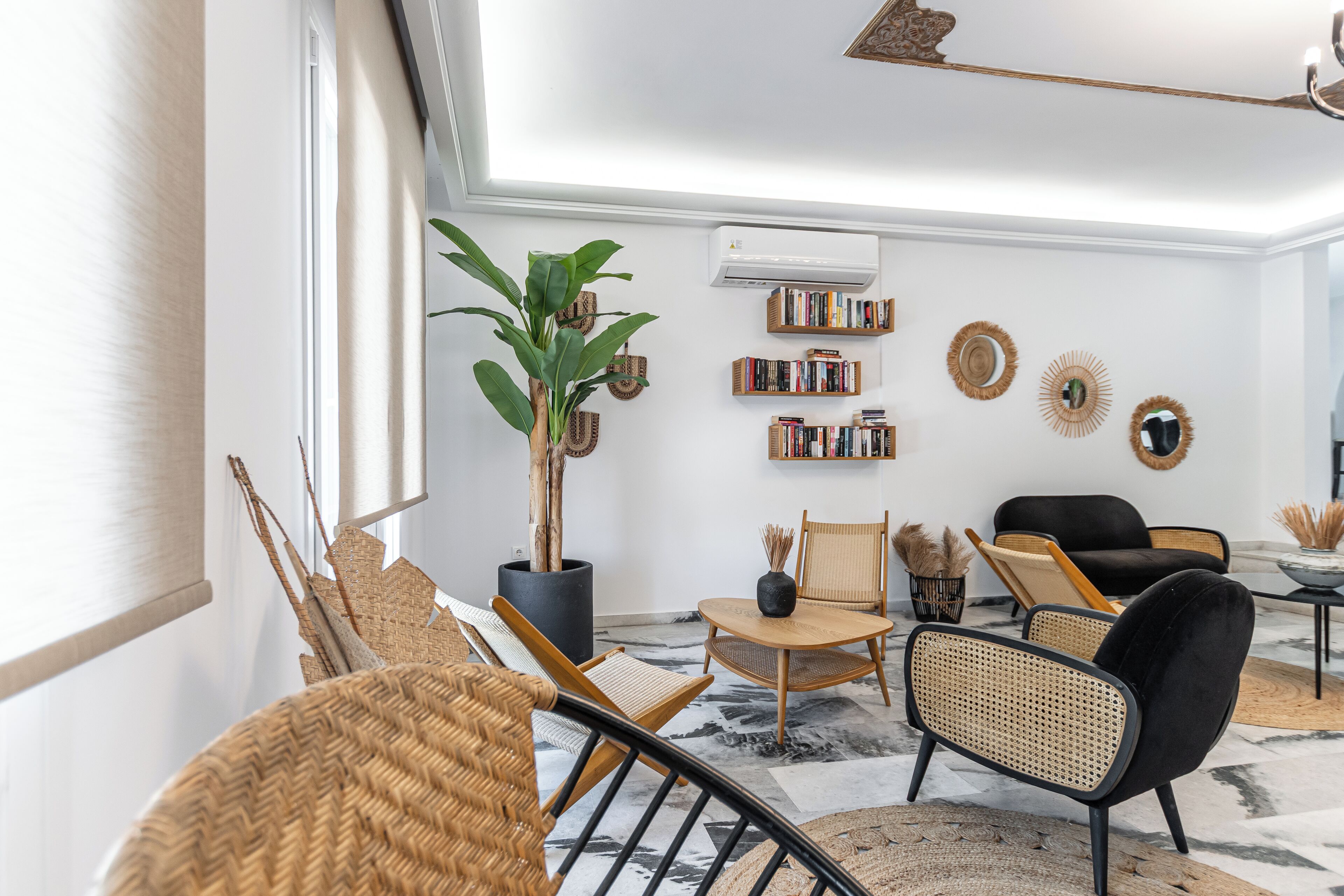 A modern living room with a large window, a potted plant, a bookshelf, and a black sofa.
