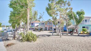 A beachside property with a sandy area, palm trees, and colorful buildings in the background. - Coral Harbour Beach House And Villas (Nassau)