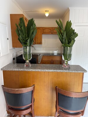 Compact kitchen with a wooden island and potted plants, featuring a stainless steel sink and wooden cabinets.