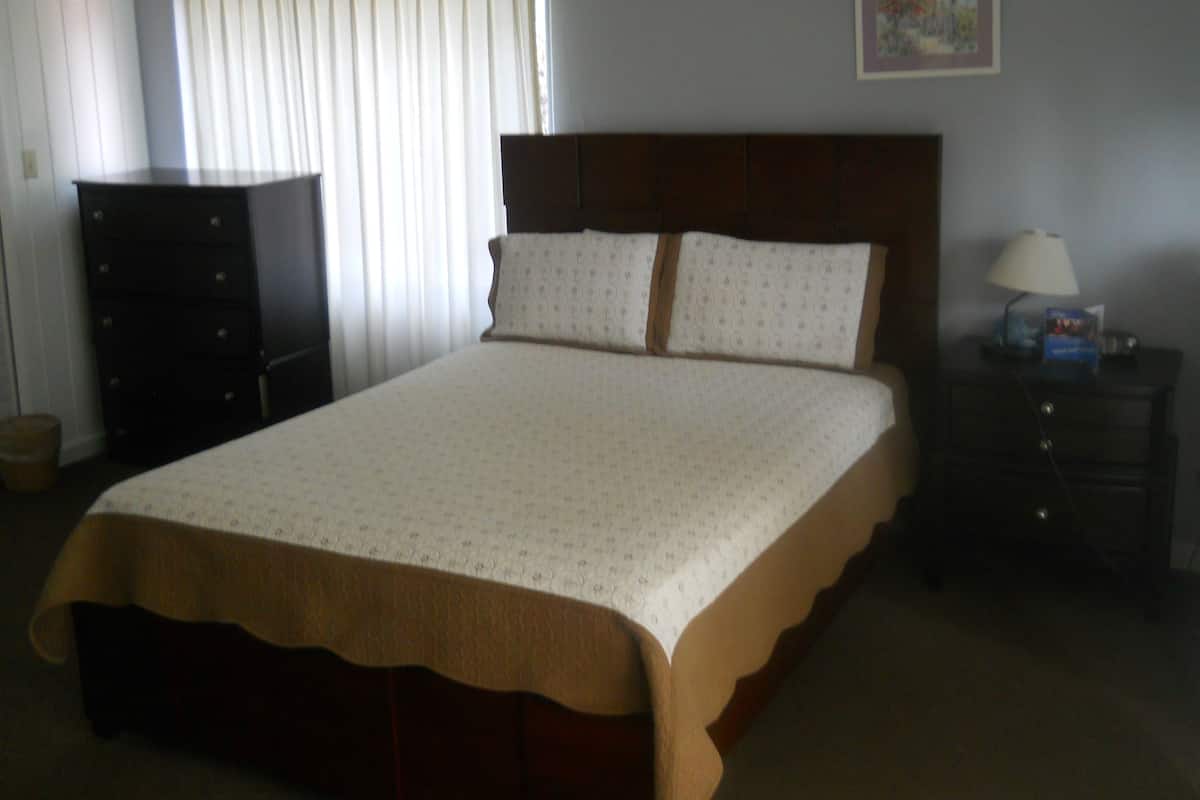 Un dormitorio con una cama grande, un aparador, una mesita de noche y una ventana con cortinas.