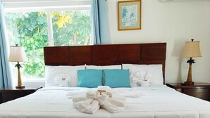 A hotel room with a large bed, two nightstands, a window with curtains, and a framed picture on the wall. - Coral Harbour Beach House And Villas (Nassau)