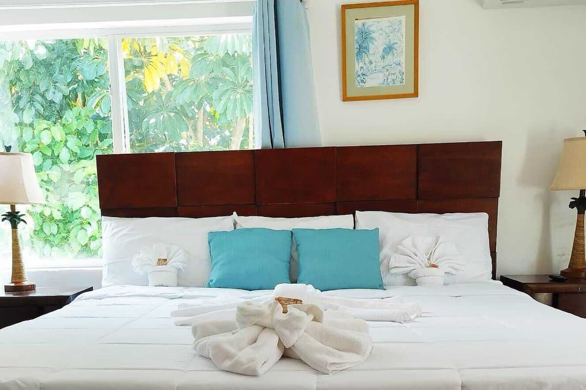 Una habitación de hotel con una cama grande, dos mesitas de noche, una ventana con cortinas y un cuadro en la pared.