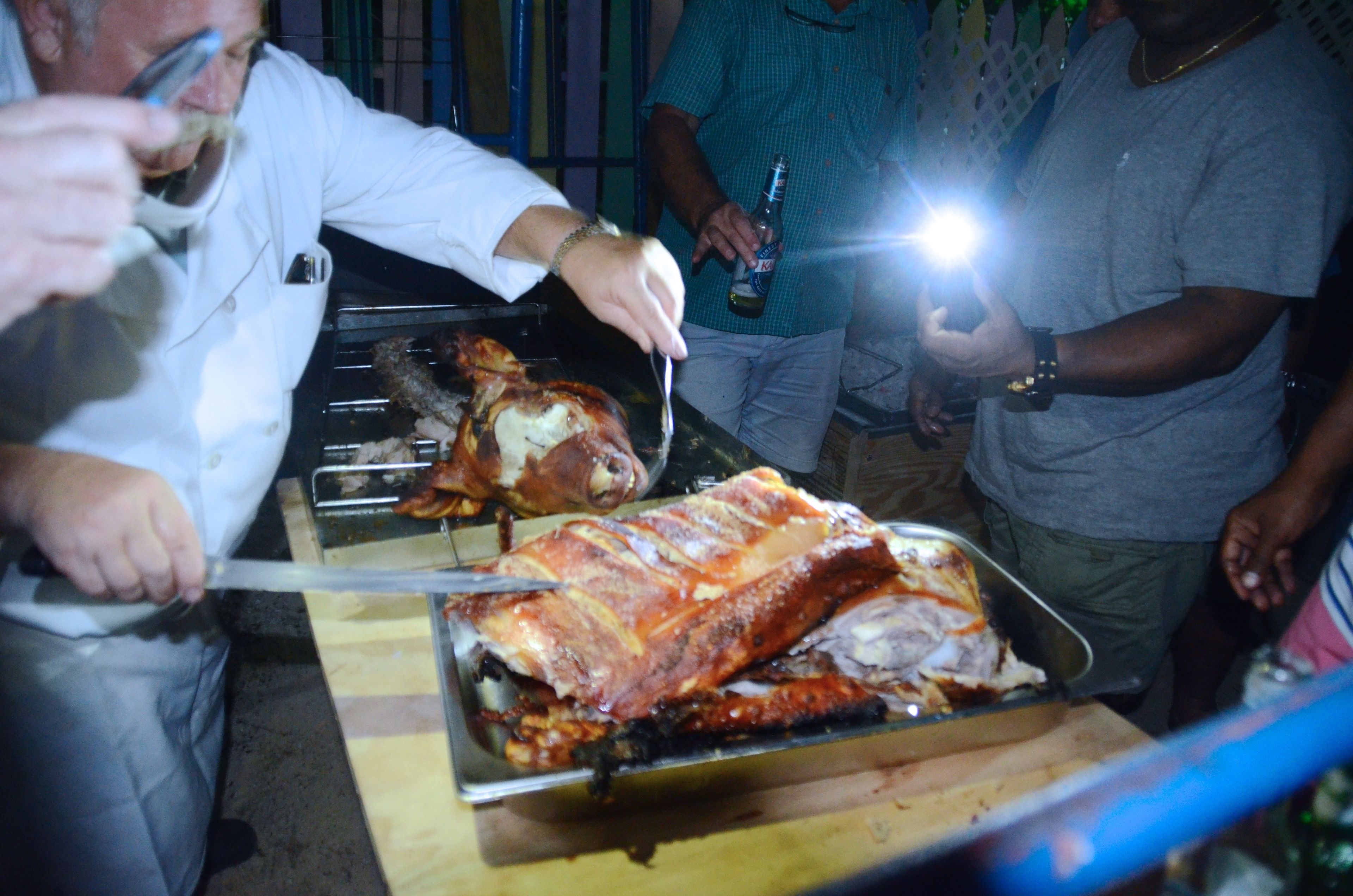 Un gros cochon rôti, présenté sur un plateau en métal, et découpé par une personne portant une chemise blanche.