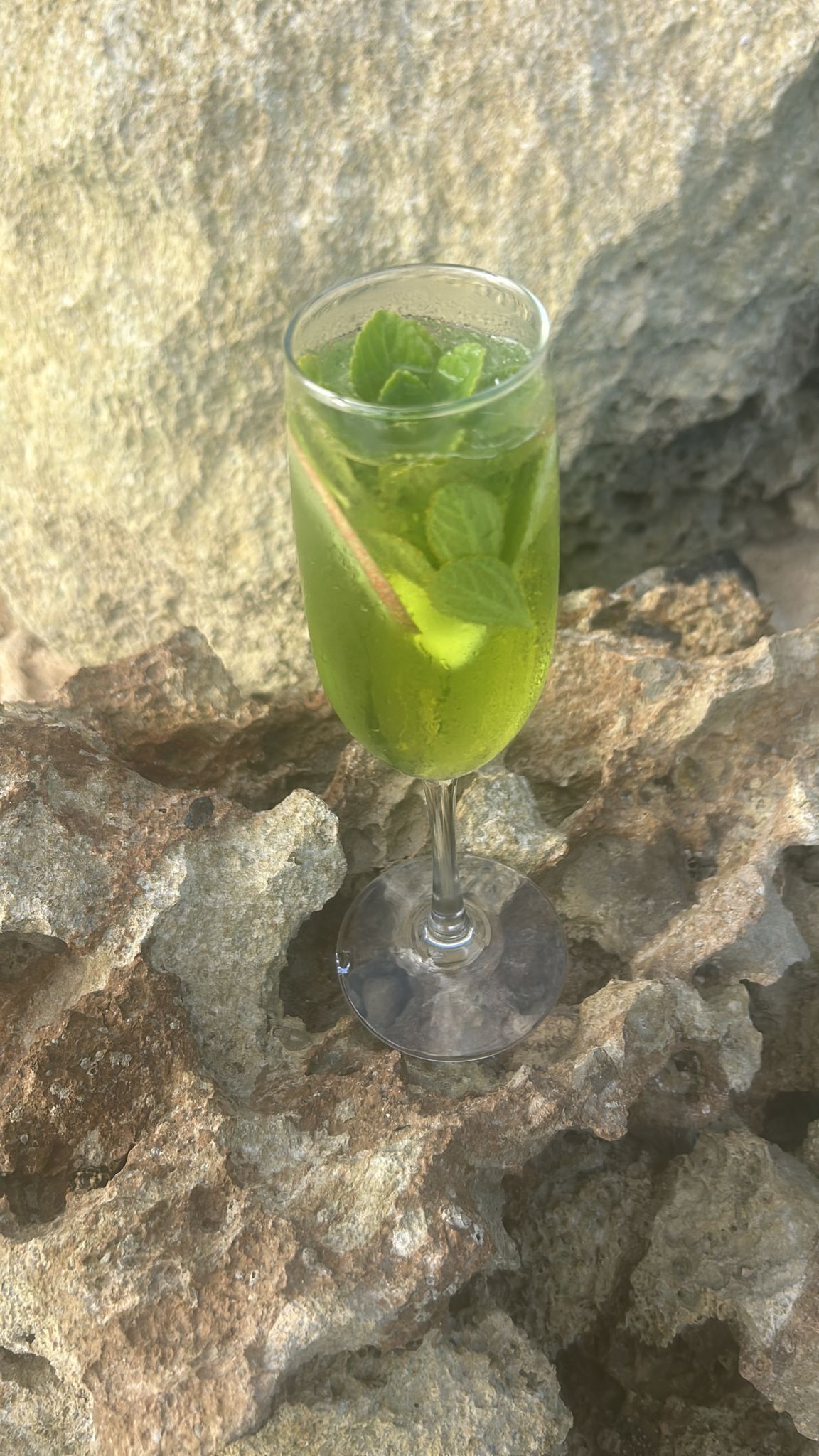 A glass of green beverage with mint leaves on a stone surface.