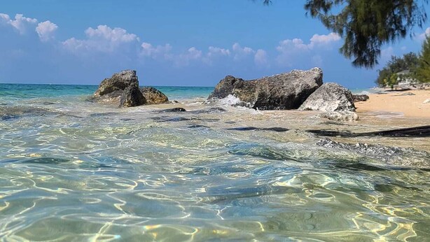 A beach with clear shallow waters, rocky outcrops, and a tree line. - Coral Harbour Beach House And Villas (Nassau)