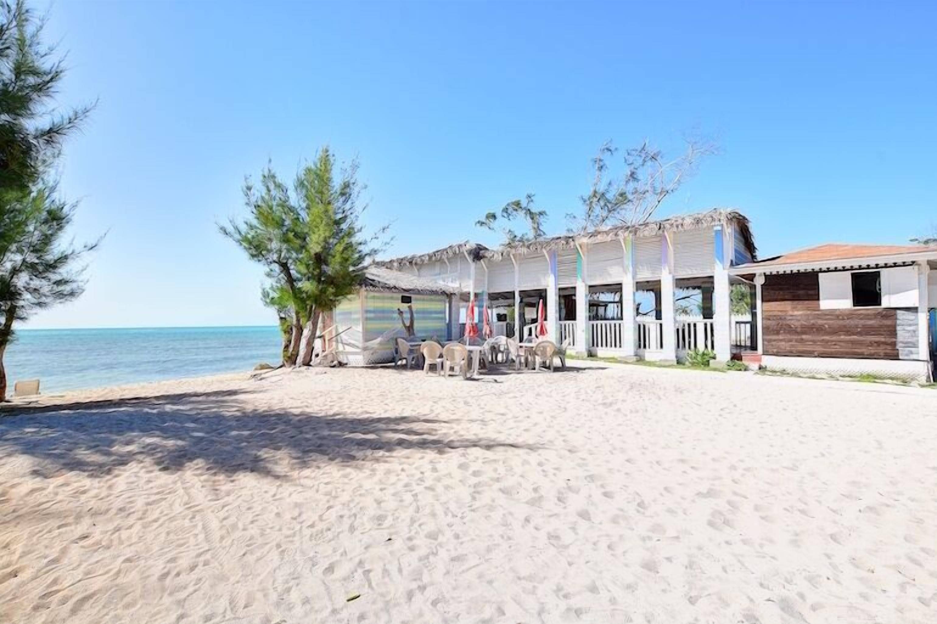 Un edificio frente a la playa con un porche cubierto, mobiliario exterior y vista al océano.