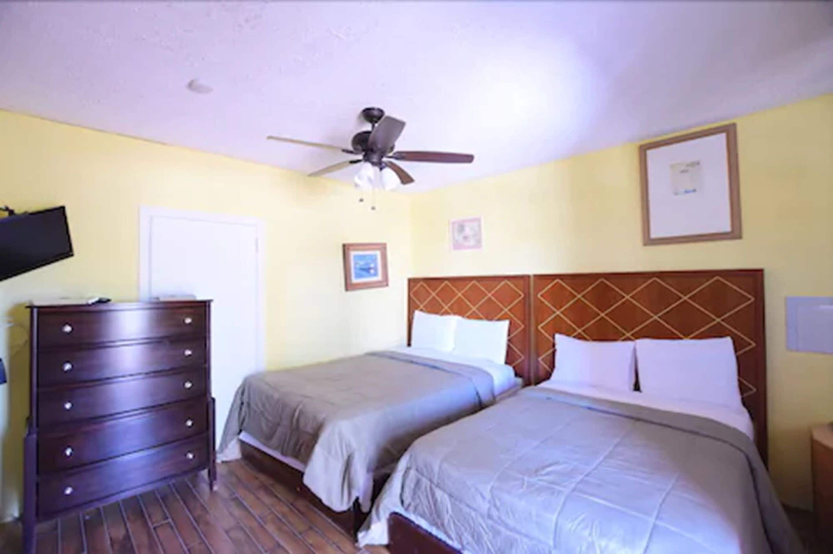 A hotel room with two beds, a ceiling fan, a dresser, and a television.