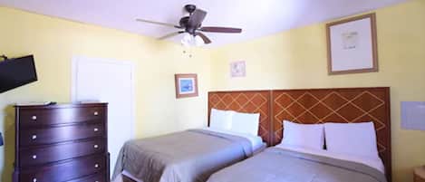 A hotel room with two beds, a ceiling fan, a dresser, and a television.