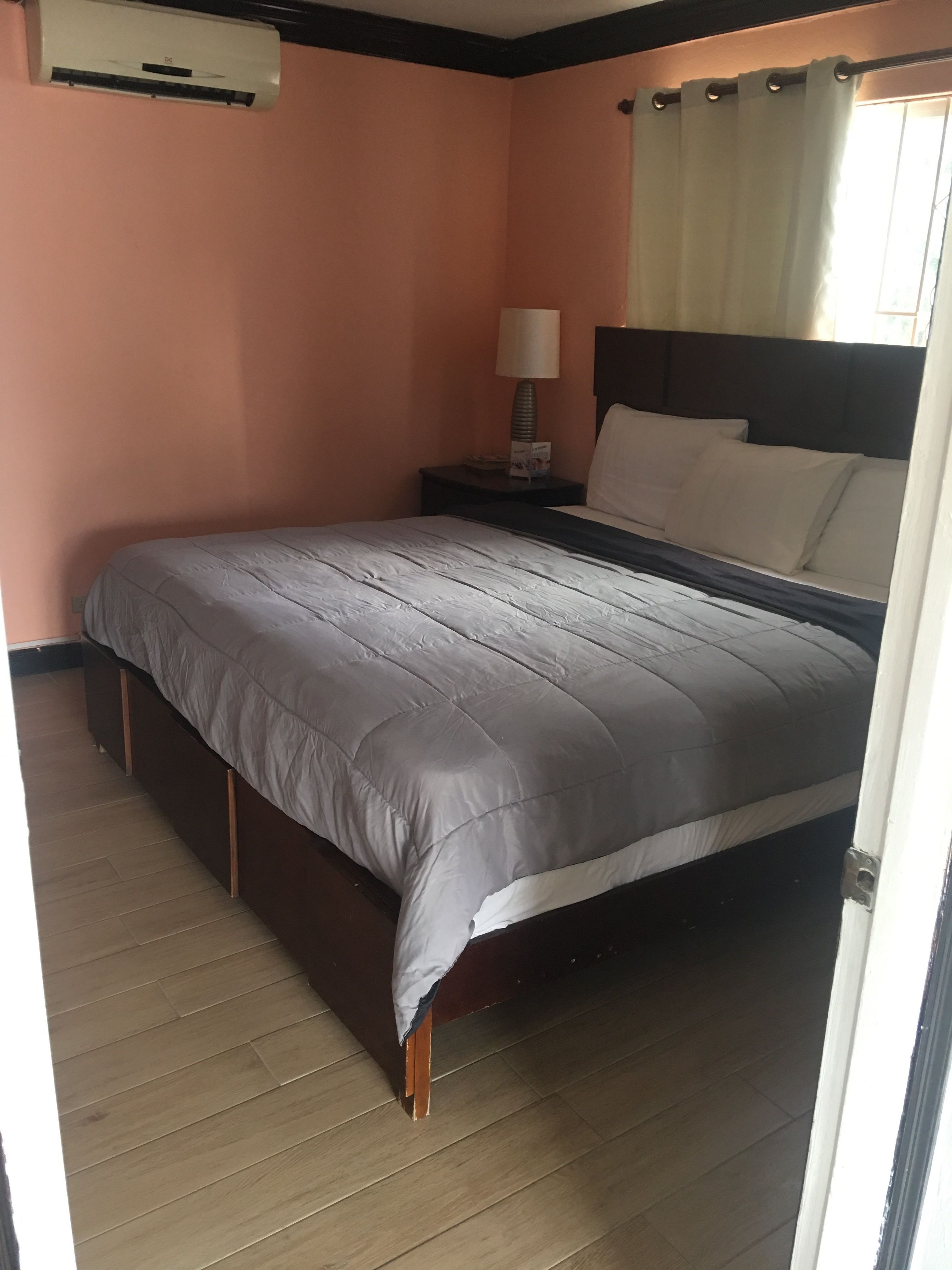 Un dormitorio con cama, mesita de noche, lámpara y aire acondicionado.