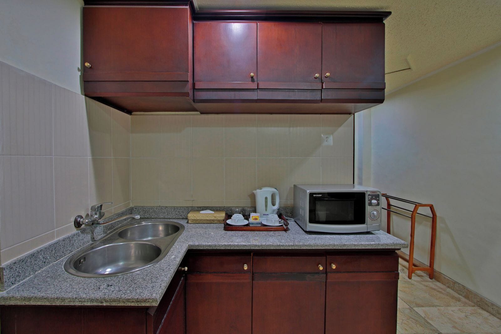 A compact kitchen with a double sink, a microwave, and wooden cabinets.