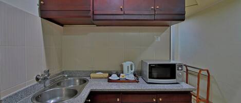 A compact kitchen with a double sink, a microwave, and wooden cabinets.