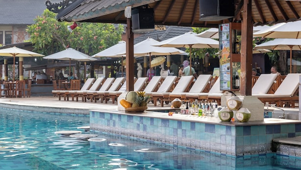 A poolside bar with lounge chairs and umbrellas, a tiled pool, and a tropical setting. - The Jayakarta Bali (Legian)