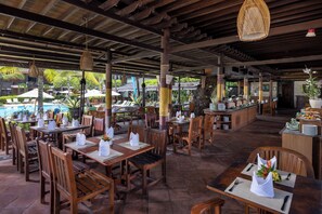 A restaurant with wooden tables and chairs, a pool in the background, and a tropical garden view. - The Jayakarta Bali (Legian)