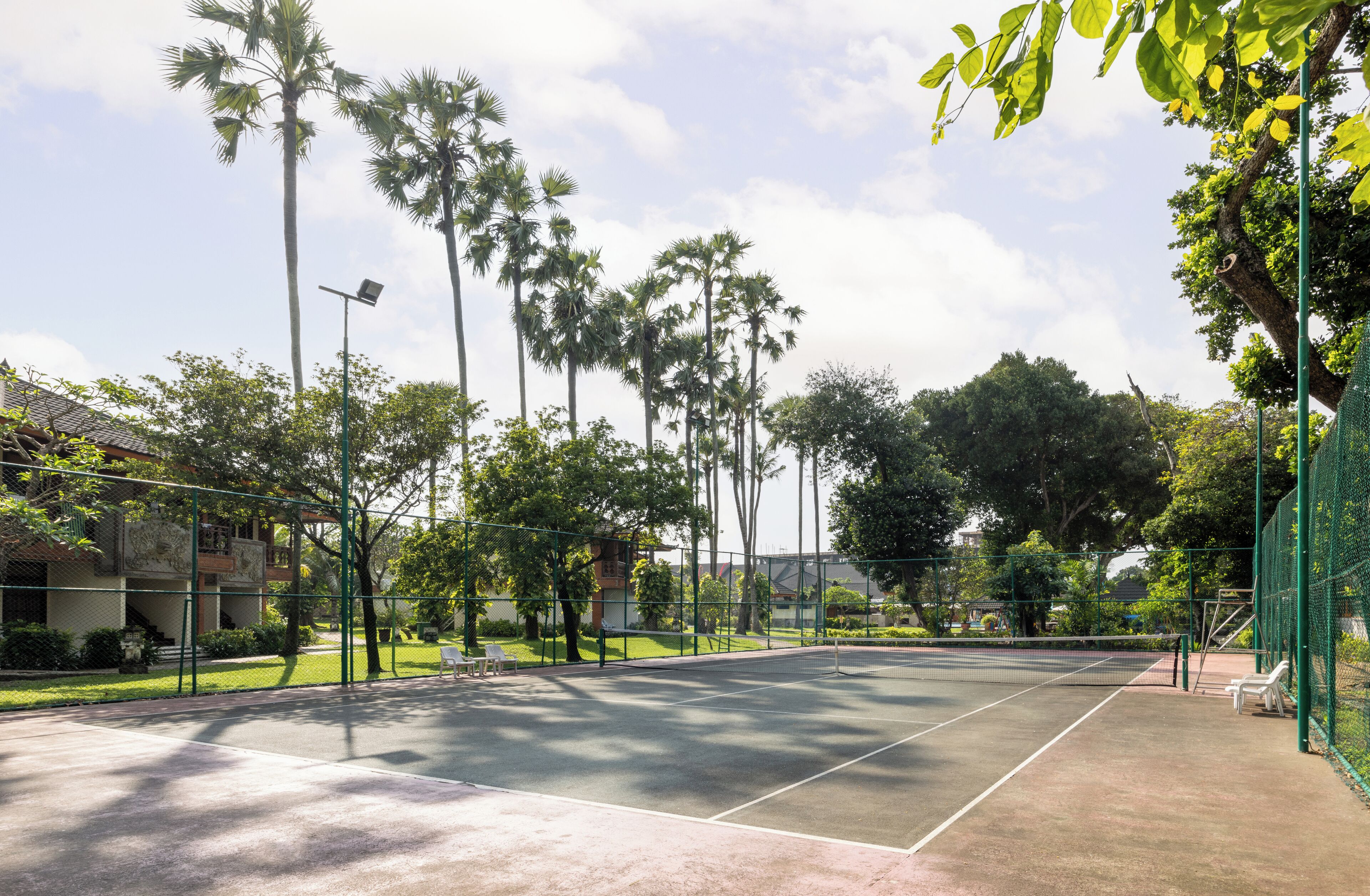 A tennis court with a net, surrounded by trees and a fence.