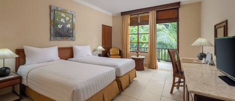 A hotel room with two beds, a television, a desk, a chair, a lamp, a painting, and a window with a view of greenery.