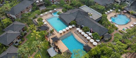 An aerial view of a resort with multiple swimming pools, lounge areas, and lush greenery.