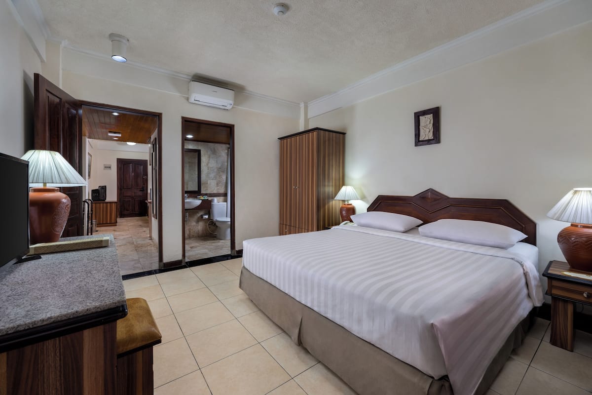 A hotel room with a bed, a TV, a desk, and a bathroom visible through an open door.