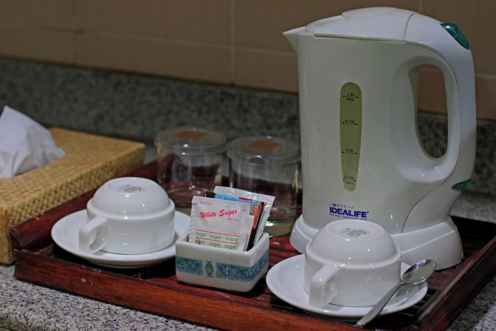 Een keuken met een witte elektrische waterkoker, een theeset en een zakje witte suiker.