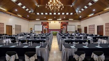 Un salón de conferencias con filas de mesas, sillas y una araña.